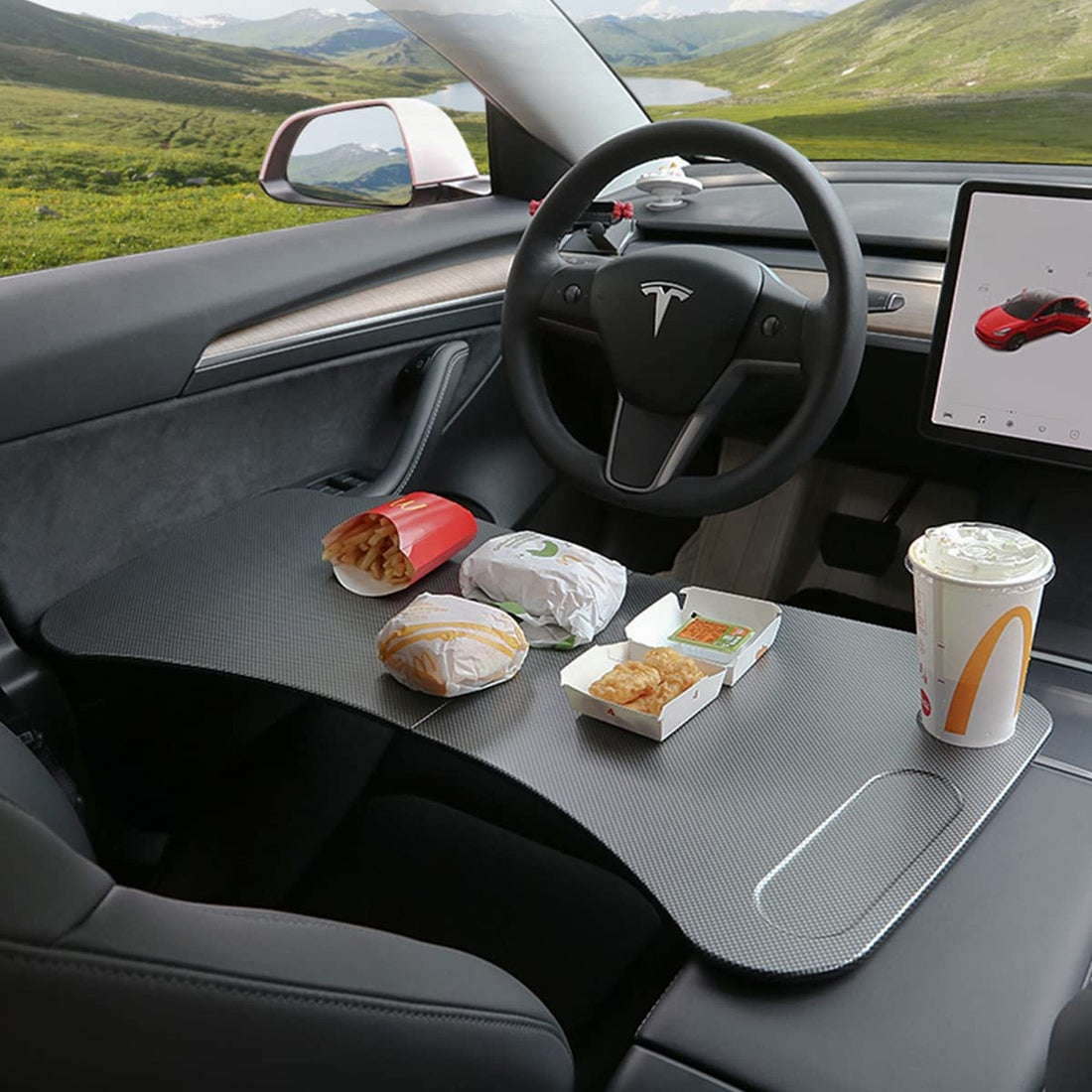 Foldable laptop desk holding a meal across the front cabin of a parked Tesla Model 3