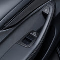 Black door panel with carbon-weave trim around four window switches and covers at the door-release controls.