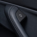 Close-up of a carbon-weave door-release cover with a white door symbol beside a stitched black grab handle.