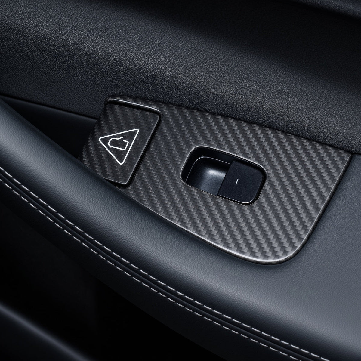 Carbon-weave surround around a single window switch and adjacent triangular door-release button on a black door panel.