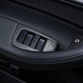 Carbon-weave driver-door switch surround viewed across the grab handle, showing four window switches and release-button covers.