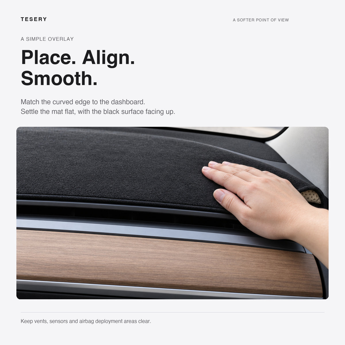 A hand smooths the black flannel mat on a legacy Tesla dashboard, with the wood trim and cabin air outlet below.
