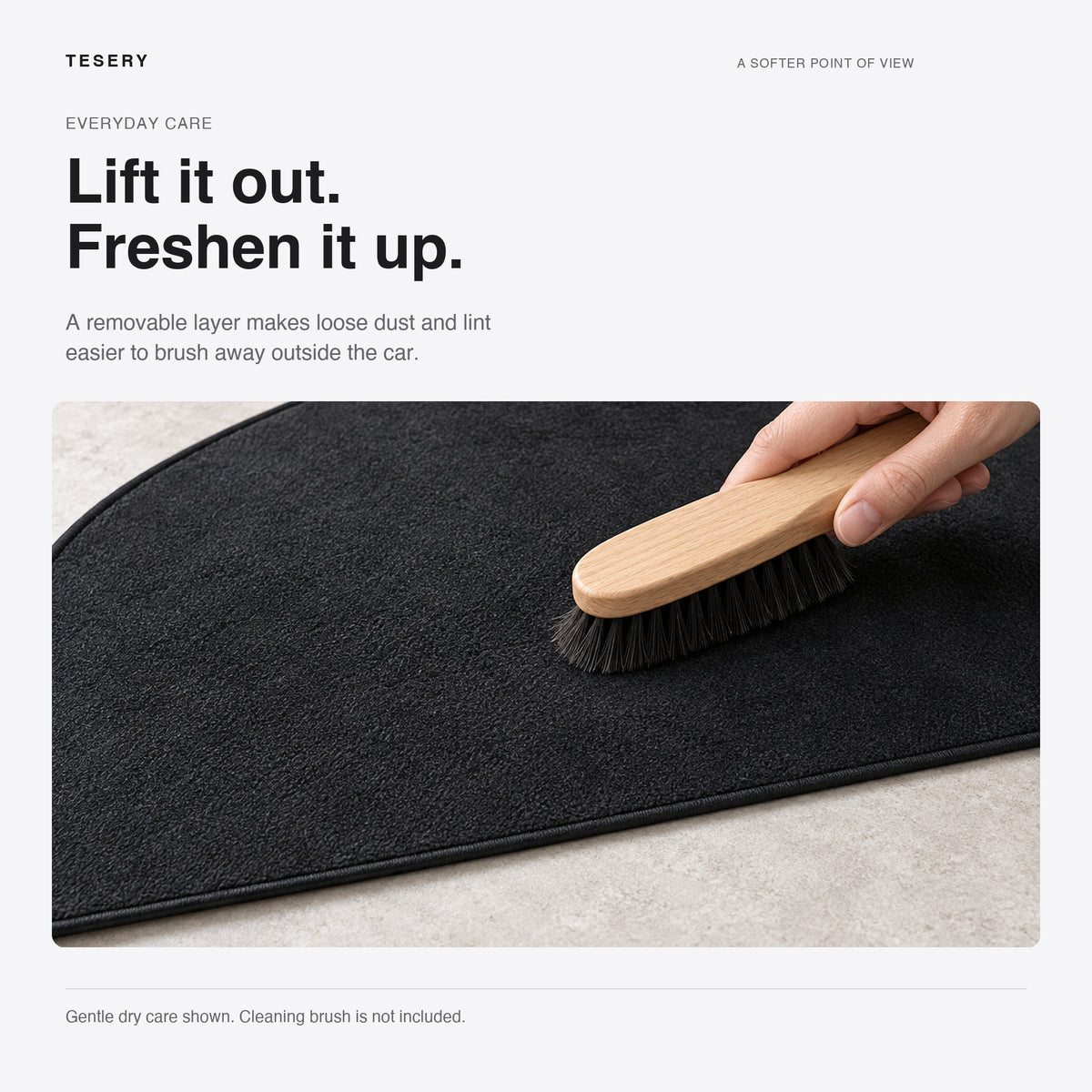 A soft brush lifts loose lint from the black flannel dashboard mat on a tabletop outside the vehicle.