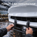 Hands aligning a black plate bracket at the lower grille of a white Model 3.